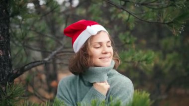 Kırmızı Noel Baba şapkalı neşeli genç bir kadın orman manzarasının keyfini çıkarıyor.