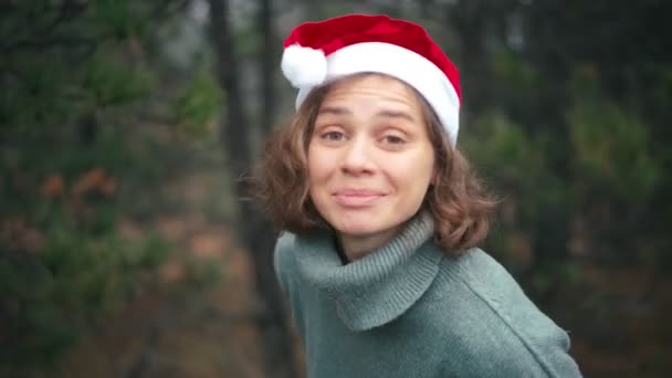 Una joven con un sombrero rojo de Santa Claus grabando un video con saludos navideños — Vídeo de stock