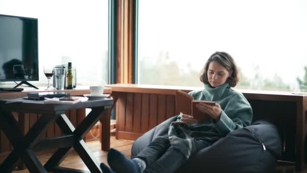 Młoda kobieta siedząca w salonie i czytająca książkę — Wideo stockowe