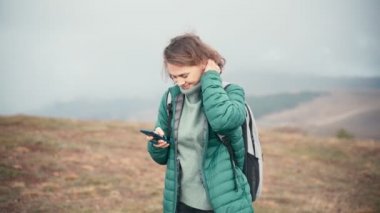 Sırt çantasıyla tepede akıllı telefonunu kullanan neşeli genç bir kadın.