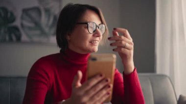 Gözlüklü neşeli genç bir kadın akıllı telefonuyla görüntülü görüşme yapıyor..