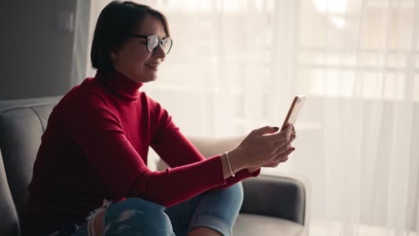Wesoła młoda kobieta w okularach odbiera wideo rozmowę ze smartfonem. — Wideo stockowe