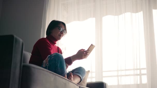 Une jeune femme joyeuse dans des lunettes prend un appel vidéo avec son smartphone. — Video