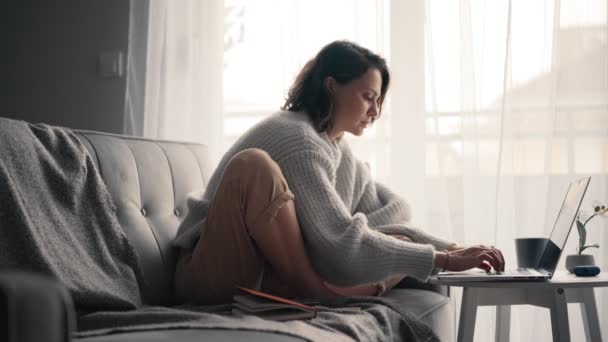 A young woman typing on a laptop, and checking messages on a smartphone — Stock Video