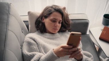 Kanepede uzanırken akıllı telefonunu kullanan rahat bir genç kadın..