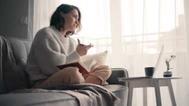 Genç ve neşeli bir kadın video görüşmesiyle konuşuyor ve not defterine not alıyor.. 