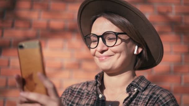 Wanita melihat ponselnya saat mendengarkan musik dengan earphone nirkabel — Stok Video