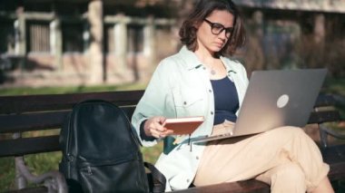 Parktaki bankta oturan ve bilgisayarında yazan genç bir kız öğrenci.
