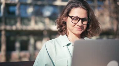 Gözlüklü, genç ve neşeli bir bayan öğrenci laptopunda çalışıyor ya da çalışıyor.