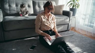 Oyuncak kedisi kanepede yatarken dizüstü bilgisayarda çalışan güzel bir kadın.