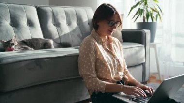 Oyuncak kedisi kanepede yatarken dizüstü bilgisayarda çalışan güzel bir kadın.