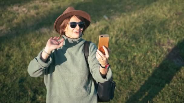 Şapkalı, orta yaşlı güzel bir kadın akıllı telefonuyla video görüşmesi yapıyor. — Stok video