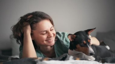 Genç bir kadının Basenji köpeğini yatakta okşarken yakın plan fotoğrafı.