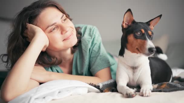 En ung kvinna slappnar av och drömmer medan hon ligger i sängen med sin hund — Stockvideo