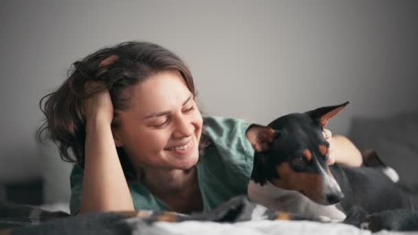 Gros plan d'une jeune femme caressant son chien basenji alors qu'elle était couchée au lit — Video