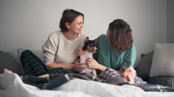 Una coppia lesbica coccola il loro cane basenji carino mentre si siede sul letto — Video Stock
