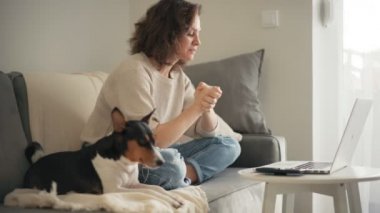 Bir kadın, köpeğiyle kanepede otururken dizüstü bilgisayarından bir video alıyor.