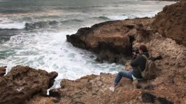 Bir fotoğrafçı kayalara çarpan büyük dalgaların fotoğraflarını çekiyor.