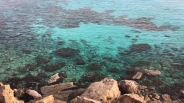 Kayalık bir sahilden kristal mavisi su yüzeyine küçük dalgalı bir manzara.