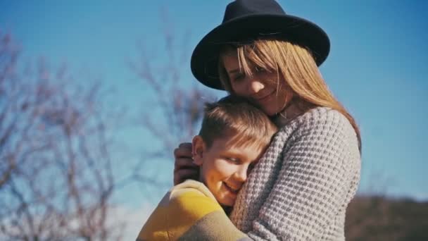 Güneşli bir günde parkta yürürken çocuğunu kucaklayan genç bir anne. — Stok video