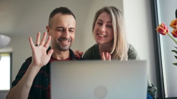 Una pareja alegre haciendo una videollamada con amigos o familiares en un portátil — Vídeo de stock