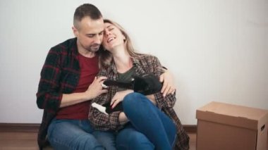 Yetişkin bir çift beyaz duvarın yanında oturmuş kediye sarılıyor.