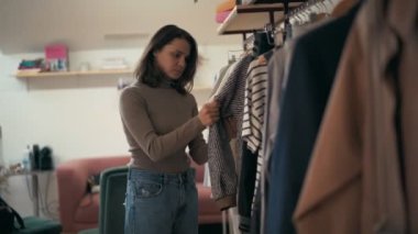 Genç bir kadın mağazadaki elbise askılarını inceliyor.