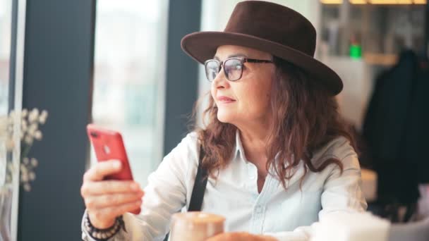 Vacker mogen snygg kvinna i hatt och glasögon med hjälp av sin smartphone — Stockvideo