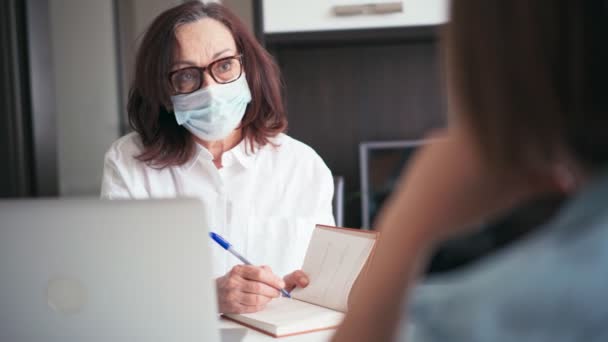 Una doctora madura usando mascarilla médica consultando a un paciente — Vídeos de Stock