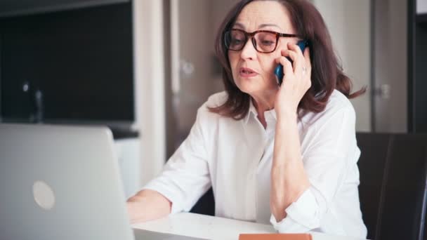 Senior mulher consultar um paciente por telefone e olhando para a tela do laptop — Vídeo de Stock