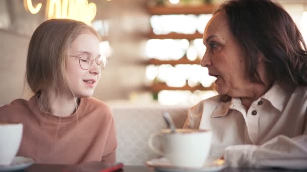 カフェに座っている間、幸せな祖母とかわいい孫娘が話しています. — ストック動画