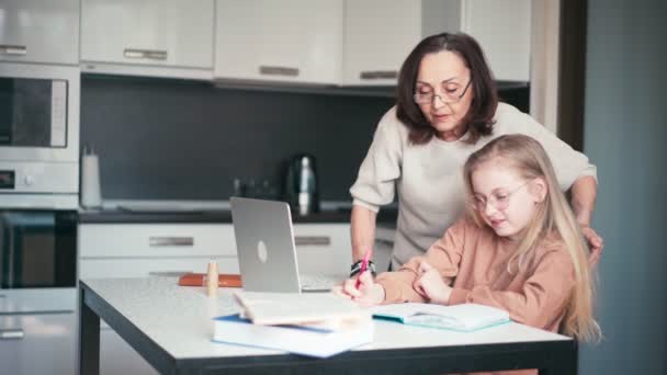 Eine freundliche Großmutter mit Brille hilft ihrer Enkelin bei den Hausaufgaben — Stockvideo