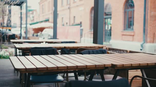 Tables en bois sur la véranda de rue vide du restaurant, les gens passent devant — Video