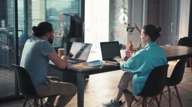 İki iş arkadaşı dizüstü bilgisayarlarının önünde oturmuş bir projeyi tartışıyorlar.