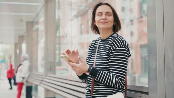 A young adult woman looking at the smartphone screen while waiting for a bus — Stock Video