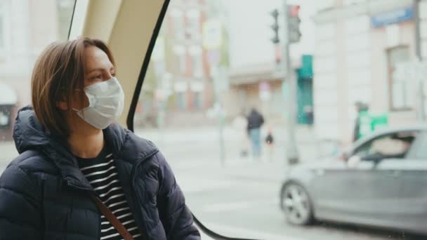 Молода жінка в масці для обличчя дивиться на вікно під час їзди на автобусі — стокове відео