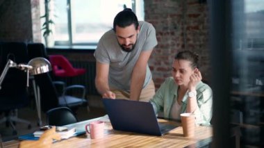 İki iş arkadaşı dizüstü bilgisayarlarının önünde oturmuş bir projeyi tartışıyorlar.