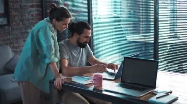 İki iş arkadaşı dizüstü bilgisayarlarının önünde oturmuş bir projeyi tartışıyorlar.