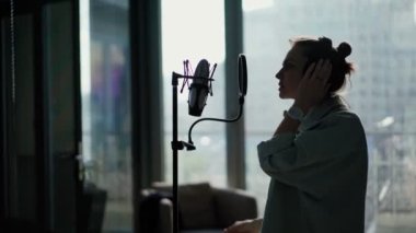 Kulaklıklı genç bir kadın mikrofona şarkı söylüyor.