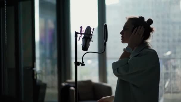 Mladá žena se sluchátky zpívá do mikrofonu na stojanu — Stock video