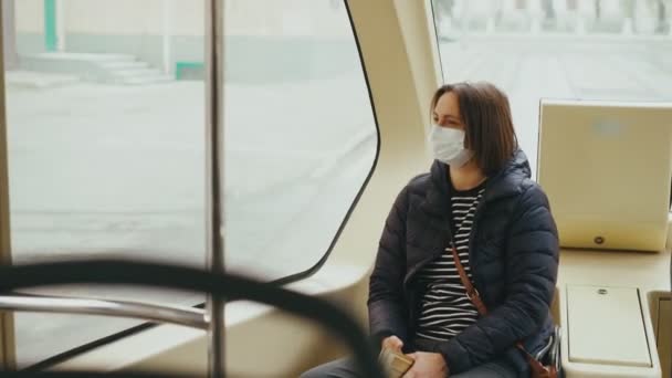 Молода жінка в масці для обличчя дивиться на вікно під час їзди на автобусі — стокове відео
