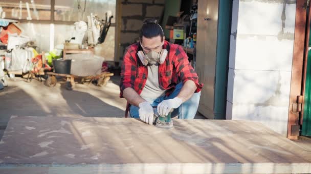 A young man in a construction respirator grinds a parquet board with a sander — Stock Video