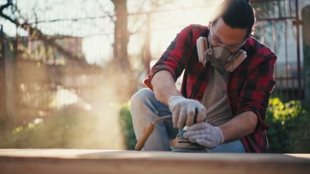 Un giovane in un respiratore da costruzione macina una tavola da parquet con una levigatrice — Video Stock