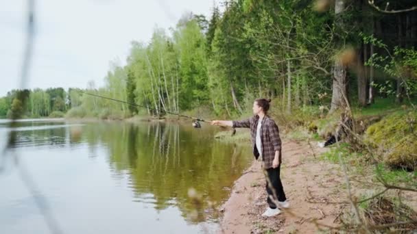 En vacker ung kvinna i rutig skjorta fiskar på sjön — Stockvideo
