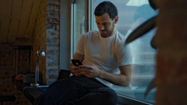 Yakışıklı bir adam geniş bir pencere pervazında oturur ve akşam manzarasının tadını çıkarır.