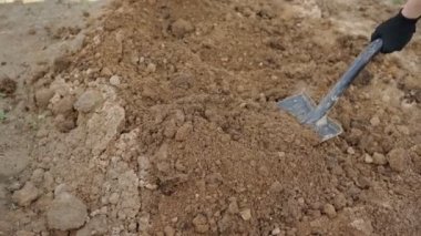 Kotlu ve iş eldivenli bir adam kürekle toprağı kazıyor..