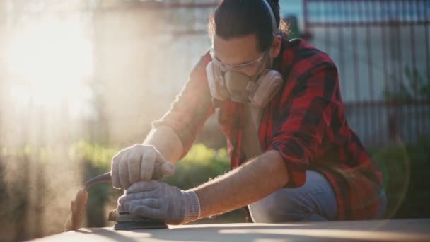 A young man in a construction respirator grinds a parquet board with a sander — Stock Video