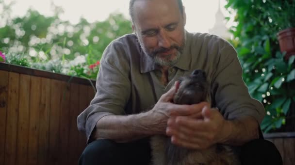 En stilig man smeker sin hund när han sitter på en öppen terrass. — Stockvideo