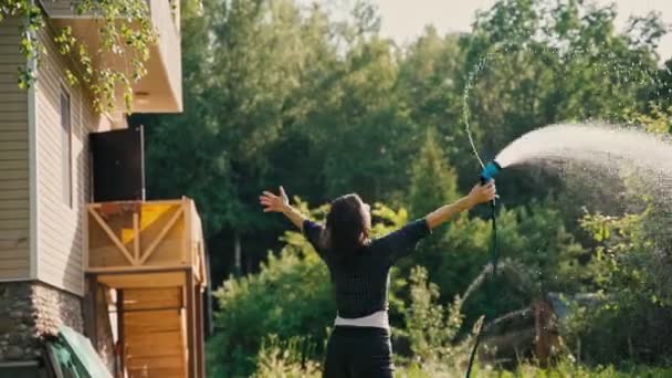 Una hermosa mujer feliz se refresca vertiendo agua sobre sí misma de una manguera — Vídeos de Stock