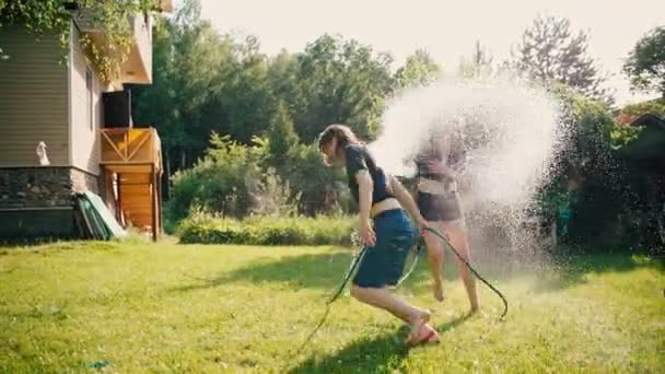Två unga kvinnor har kul med att stänka varandra med vatten från slangar — Stockvideo